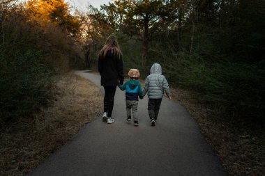 Doğa ile çevrili bir yolda yürürken üç kardeş el ele tutuşur.