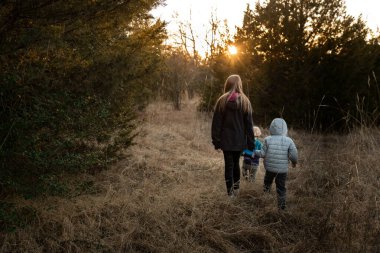 Üç çocuk ormanda gün batımına doğru kuru çimenlerde yürüyor.