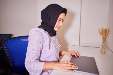 Masada dizüstü bilgisayar kullanan Asyalı Müslüman kadın.