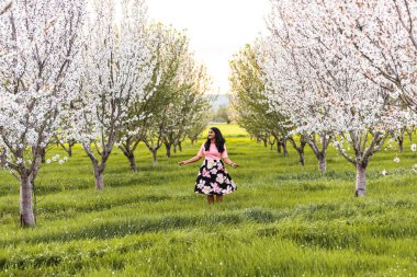 Bahar zamanı çiçek açan bir badem bahçesinde neşeyle dikilen bir kadın.