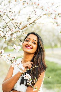 Gülümseyen kadın beyaz bir elbise içinde dalların arasında poz veriyor..