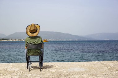 Deniz kıyısındaki bir sandalyede oturan birinin arka görüntüsü.