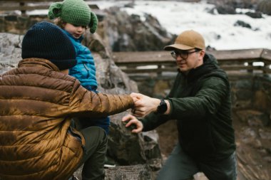 Baba, yeni yürümeye başlayan oğulların sonbaharda kayadan aşağı inmelerine yardım eder.