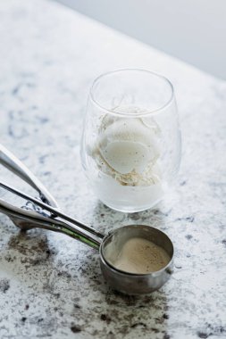 Vanilla ice cream in a glass with a scoop on a marble countertop clipart