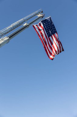 Amerikan bayrağı gökyüzünde bir itfaiye merdiveninden sarkıyor.