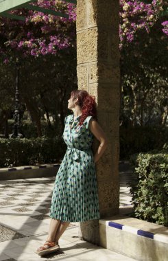 Bahçede bir sütunun yanında duran orta yaşlı bir kadın.