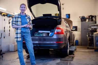 female mechanic holding work tool and standing at entrance of garage clipart