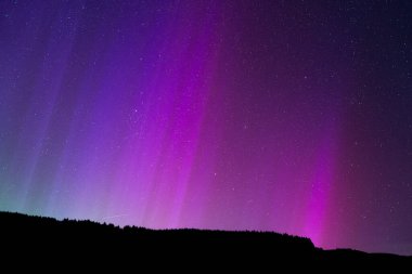 Mor ve yeşil aurora borealis bayırın üzerinde çizgiler var.