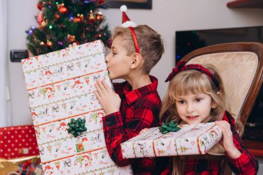 Noel kıyafetleri içinde kız ve erkek kardeşler ellerinde hediyeler tutuyorlar.