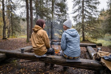 Kadın ve erkek ormanda kamp ateşi yakıyor.