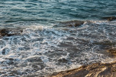 Dalgalar karanlık kaya kümelerinin üzerine düşüyor, çalkantılı okyanuslar