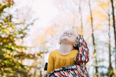 Sonbahar günü renkli battaniyeye sarılı neşeli genç çocuk.