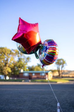 Colorful birthday balloons floating outdoors with a blue sky clipart