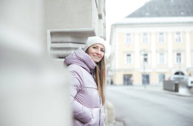 Karlı şehir caddesindeki binaya yaslanan kışlık montlu kadın.