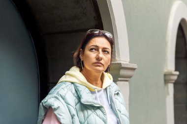 Sıradan kapüşonlu ve yelekli bir kadın kemer yolunun yanında duruyor.