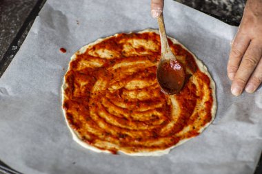Parşömen kağıdındaki pizzaya domates sosu ekleyen kişi