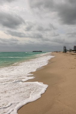 Miami sahilinde bulutlu bir gökyüzünün altında köpüklü dalgalar kıyıya vuruyor.