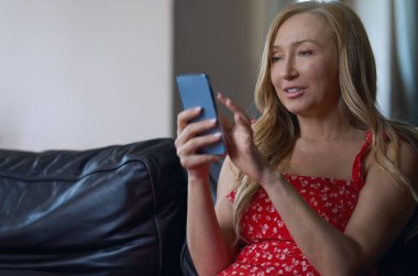 Evdeki dingin sarışın kadın kanepede dinleniyor ve akıllı telefon kullanıyor.