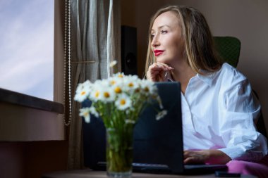 İş kadını beyaz gömlek giyiyor, laptop kullanıyor.