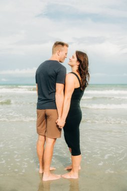 Kumsalda el ele tutuşan, yüz yüze duran bir çift.