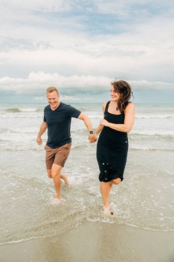 Kumsalda koşan, gülümseyen ve el ele tutuşan bir çift.
