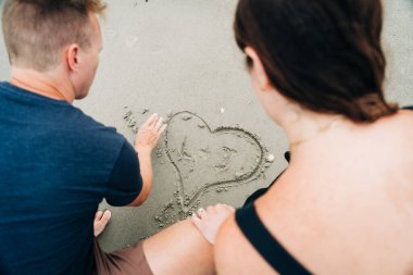 Couple drawing a heart in the sand together, with initials inside clipart