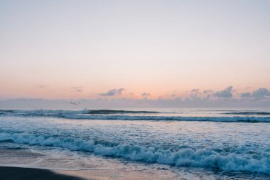Sakin dalgaların üzerinde sakin bir kumsalda yumuşak renklerle gün doğumu