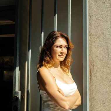 Çapraz kollu bir kadın güneş ışığında dikiliyor.