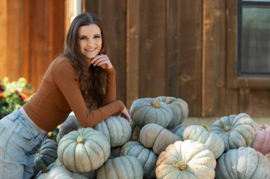 Kırsal bir çiftlik ortamında balkabaklarına yaslanan gülümseyen kadın.
