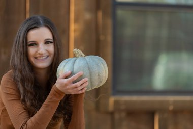 Woman holding a pumpkin at a rustic farm setting. clipart