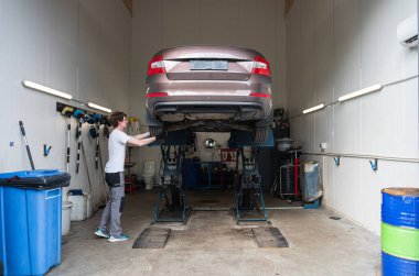 Side view of young male mechanic examining car at garage clipart