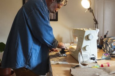 Evde dikiş makineleriyle dikiş diken bir adam.
