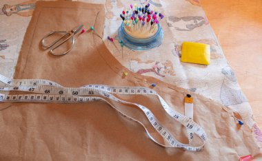 Çalışma masasında bir kalıp, iğneler ve kumaş var.