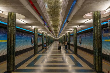 Mavi ve beyaz döşemesi olan uzun, boş bir metro istasyonu.