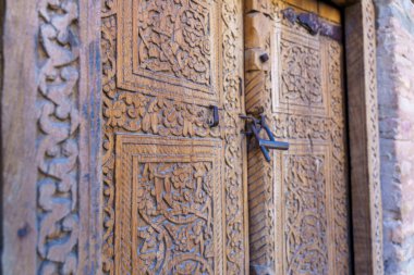 Kapı karmaşık tasarımlarla oyulmuş ve metal bir kilidi var.