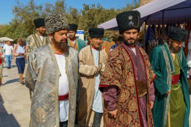 Geleneksel kıyafetler ve şapkalar giyen bir grup adam yürüyor.