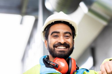 Kasklı genç mühendis sakallı fabrikanın dışında duruyor.