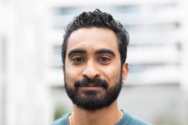 Arka planda bulanık evleri olan sakallı genç bir adamın portresi. 