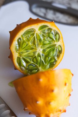 Kiwano meyvesinin yarısı görünür yeşil tohumlarla birlikte kesim tahtasının üzerinde.