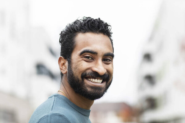 Портрет молодого человека с бородой и размытыми домами на заднем плане 