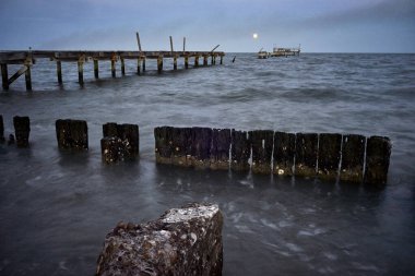 a weathered pier stretches into calm waters clipart