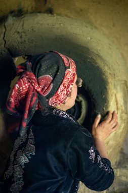 Kırmızı ve siyah atkı takan bir kadın bir deliğe bakıyor.