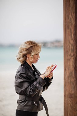 İş kadını deniz altyapısına karşı akıllı telefon kullanarak duruyor