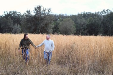 Çimen tarlasında yürürken el ele tutuşan çift
