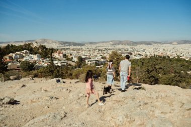 Tepede durmuş Atina şehrine bakan kızları olan baba.