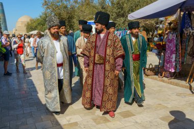Geleneksel kıyafetler giyen bir grup adam sokakta yürüyor.
