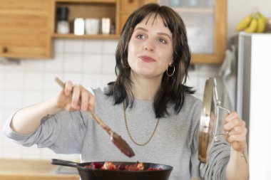 Genç bir kadın mutfakta yemek pişiriyor.