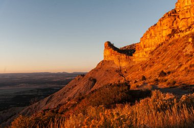 Altında engin düzlükleri olan kayalık bir uçurumun üzerinde altın saat ışığı