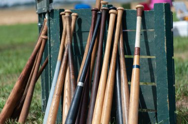 Tahta beyzbol sopaları güneşli bir kurşunun üzerinde yeşil bir sandığa yaslanıyor.