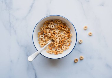 Bir kase Cheerios kahvaltı gevreği beyaz mermer üzerinde süt içinde.